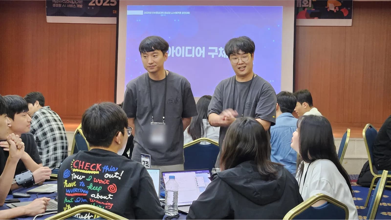 카테고리 전문가 두 명이 팀 테이블 옆에 서서 피드백을 주는 모습